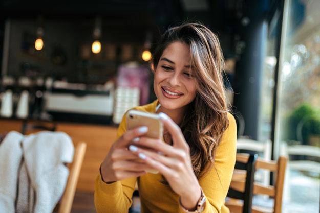 woman in restaurant smiling using mobile phone