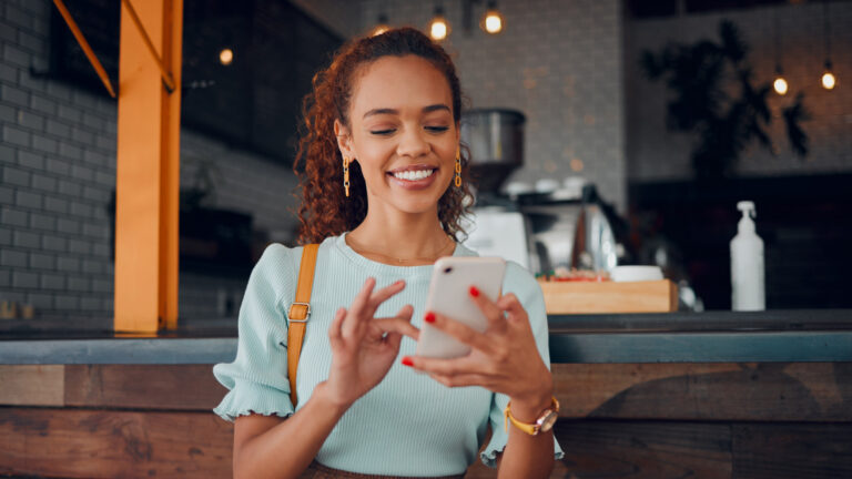 Woman smiling at her phone while sitting at a café counter